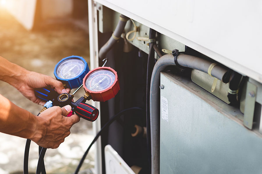 HVAC technician using manifold gauges to check refrigerant levels on an air conditioning unit