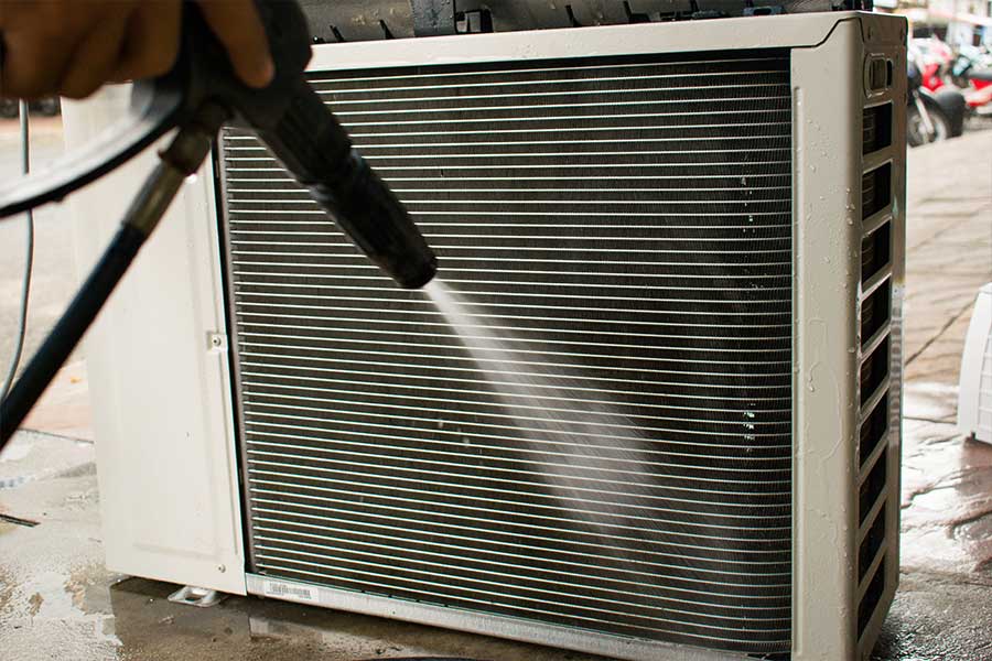 An HVAC technician cleans an outdoor unit